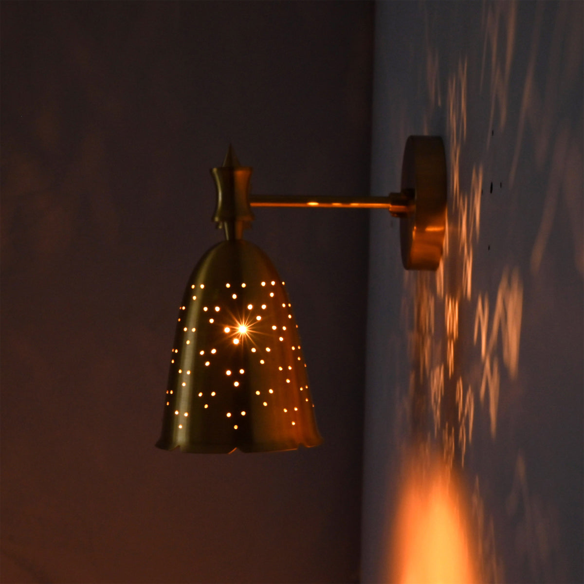 Side view of illuminated perforated bell wall sconce casting warm dotted patterns on the wall.