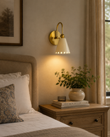 The Luna Scalloped Cone Wall Sconce installed beside a bed in a modern bedroom, providing warm ambient lighting with its white scalloped shade and solid brass finish.