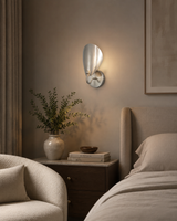 The Luna Sculptural Petal Wall Sconce installed beside a modern bedroom, providing warm ambient lighting with its sculptural satin nickel petal shade in a contemporary interior.