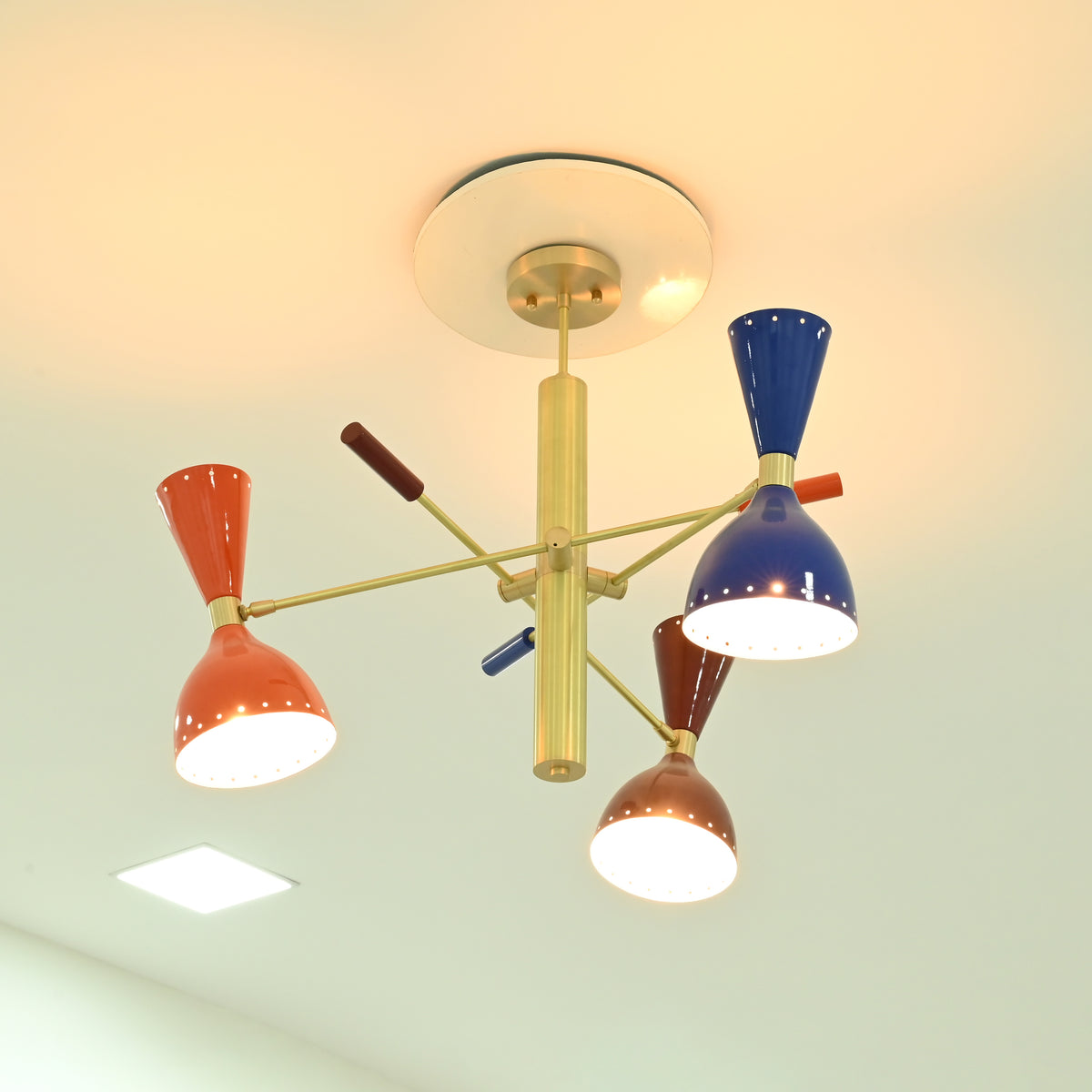 Manhattan retro Sputnik chandelier featuring illuminated orange, blue, and brown double-cone metal shades with warm lighting and brass-tone frame.