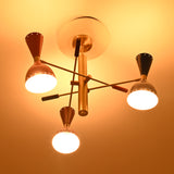 Angled night view of Manhattan retro chandelier showcasing asymmetric brass-tone arms, colorful metal shades, and bright downward illumination.