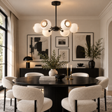 Marbella 6 light Mid-Century Modern dome chandelier illuminated above a contemporary dining table with white sculptural shades and black frame.
