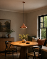 Marlow Copper Dome Pendant Light installed above a round wooden dining table in a warm modern dining room, creating inviting ambient illumination with its handcrafted copper dome shade.