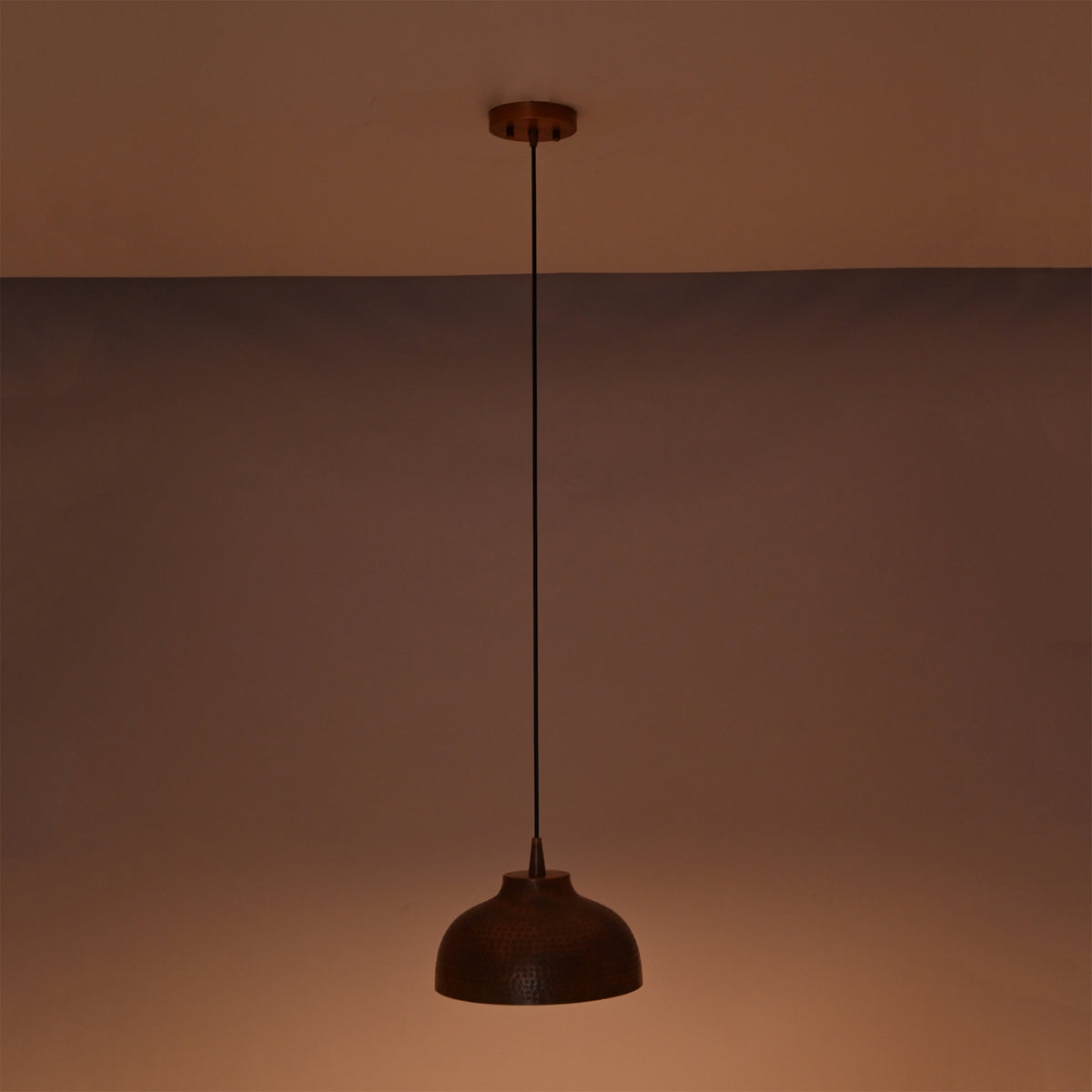 Marlow hammered copper dome pendant light suspended in a dark setting with soft ambient illumination emphasizing the handcrafted copper finish.