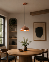 Marlow hammered copper dome pendant light installed above a modern wooden dining table in a Scandinavian-inspired dining room, providing warm ambient illumination.