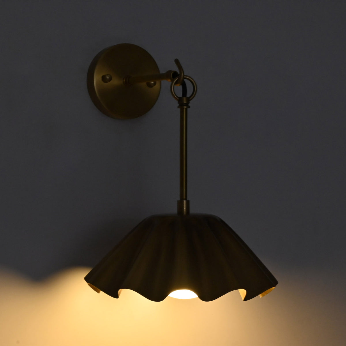 Angled illuminated view of the Marlow Modern Pleated Flower Wall Sconce featuring a handcrafted pleated flower-inspired metal shade with warm ambient illumination from the frosted opal glass globe.