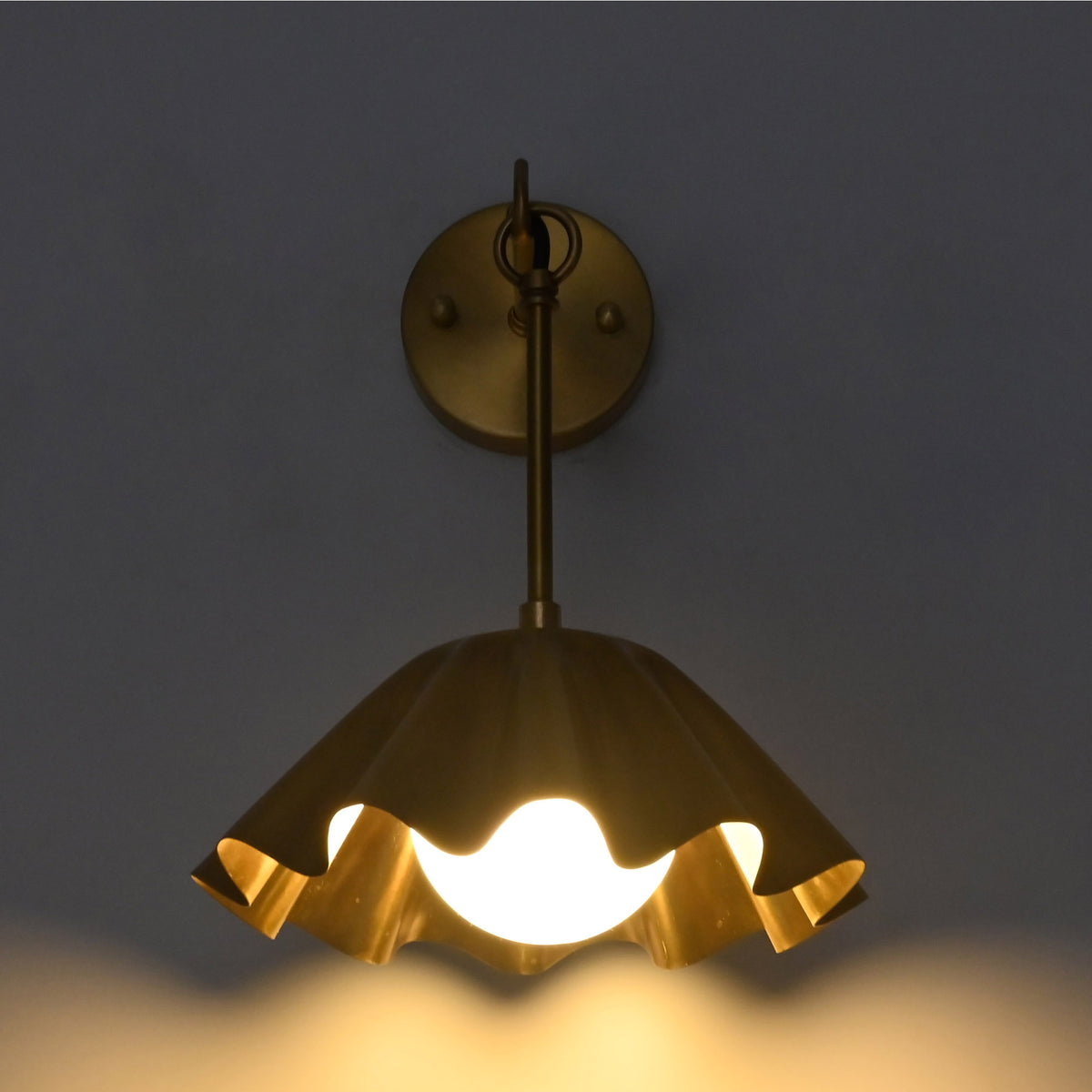Front illuminated view of the Marlow Modern Pleated Flower Wall Sconce casting a warm ambient glow through the frosted opal glass globe beneath the pleated flower-inspired shade.