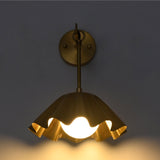 Front illuminated view of the Marlow Modern Pleated Flower Wall Sconce casting a warm ambient glow through the frosted opal glass globe beneath the pleated flower-inspired shade.