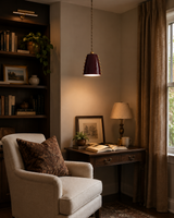 Marlow studded cone pendant light installed above a cozy reading nook, providing warm focused illumination with its glossy burgundy shade and brass decorative accents.