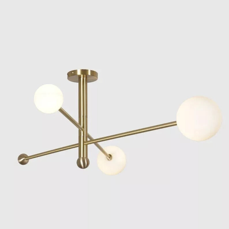 Angled view of the Marrakech 3-light chandelier featuring intersecting brass-tone metal arms, three opal white glass globes, decorative ball finials, and a sculptural Mid-Century Modern design.