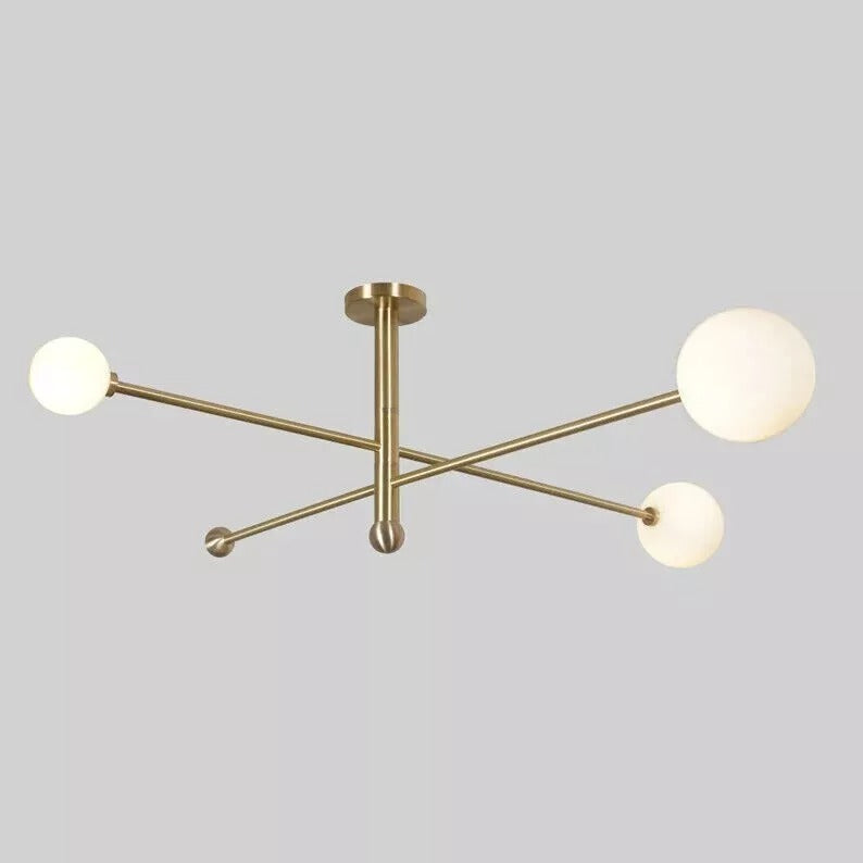 Front view of the Marrakech brass linear chandelier showcasing three spherical opal glass shades, crossed horizontal metal arms, and a central vertical ceiling stem.