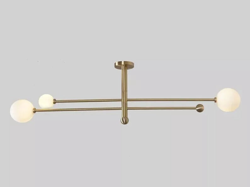 Horizontal view of the Marrakech 3-light Mid-Century Modern chandelier featuring slender brass-tone arms, three opal white globe shades, and decorative metal finials against a neutral background.