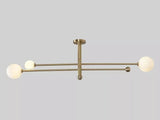 Horizontal view of the Marrakech 3-light Mid-Century Modern chandelier featuring slender brass-tone arms, three opal white globe shades, and decorative metal finials against a neutral background.