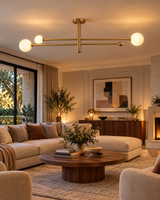 Marrakech 3-light brass globe chandelier mounted above a cream sectional sofa and round walnut coffee table in a contemporary living room with warm lighting and minimalist decor.