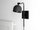 Matte black adjustable wall sconce with dome metal shade and swing arm, modern bedside reading light mounted on white wall
