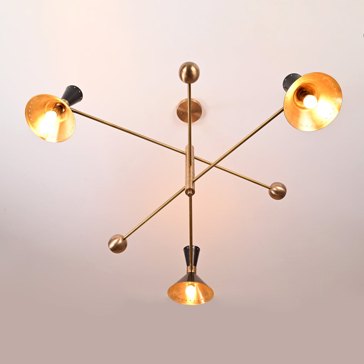Angled side view of 6 light mid-century brass chandelier with black perforated cone shades