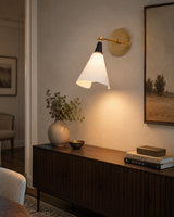 Milan Adjustable Cone Wall Sconce installed above a wooden sideboard in a modern living room, providing warm ambient lighting with its adjustable white cone shade and solid brass arm.