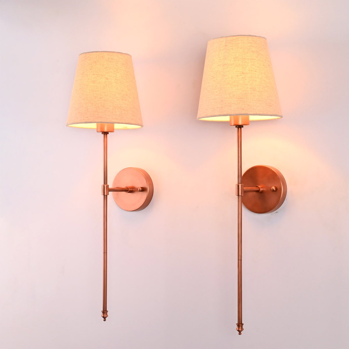 Angled view of Milan copper rod wall sconce with beige fabric shade and round wall backplate.