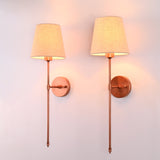 Angled view of Milan copper rod wall sconce with beige fabric shade and round wall backplate.