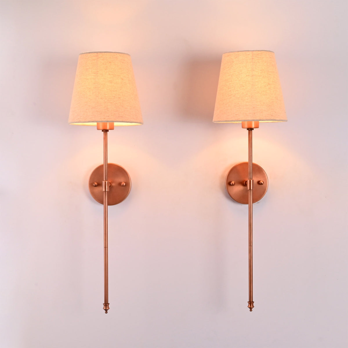 : Front view of Milan beige shade copper rod wall sconces shown as a matching pair with warm ambient glow