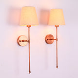 Illuminated pair of Milan copper rod wall sconces with beige shades creating soft warm wall lighting.