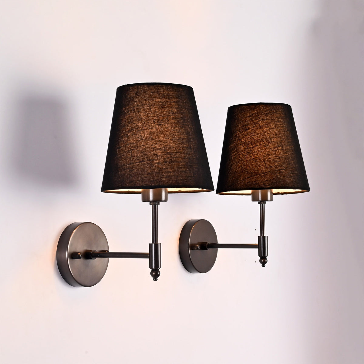Close angled view of Milan black fabric shade wall sconces with round backplates and short stems.