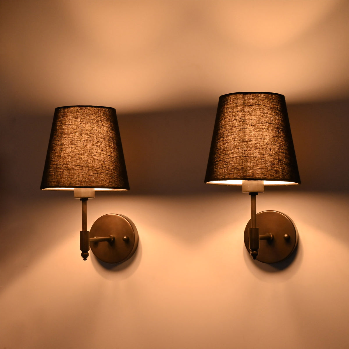 Front illuminated view of Milan black wall sconces with textured fabric shades and moody ambient glow.