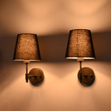 Front illuminated view of Milan black wall sconces with textured fabric shades and moody ambient glow.