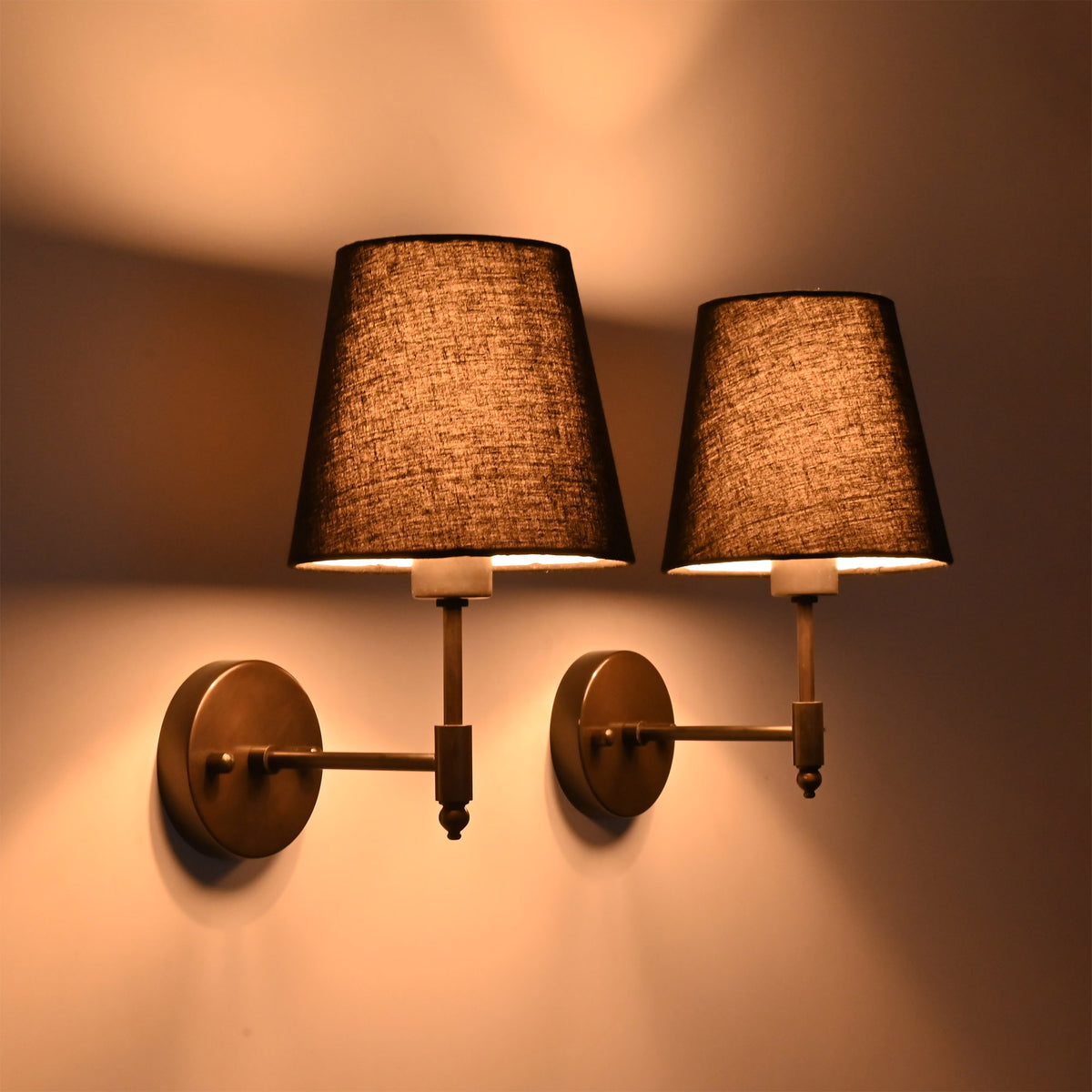 Dark room view of Milan black shade wall sconces creating warm dramatic light on the wall.