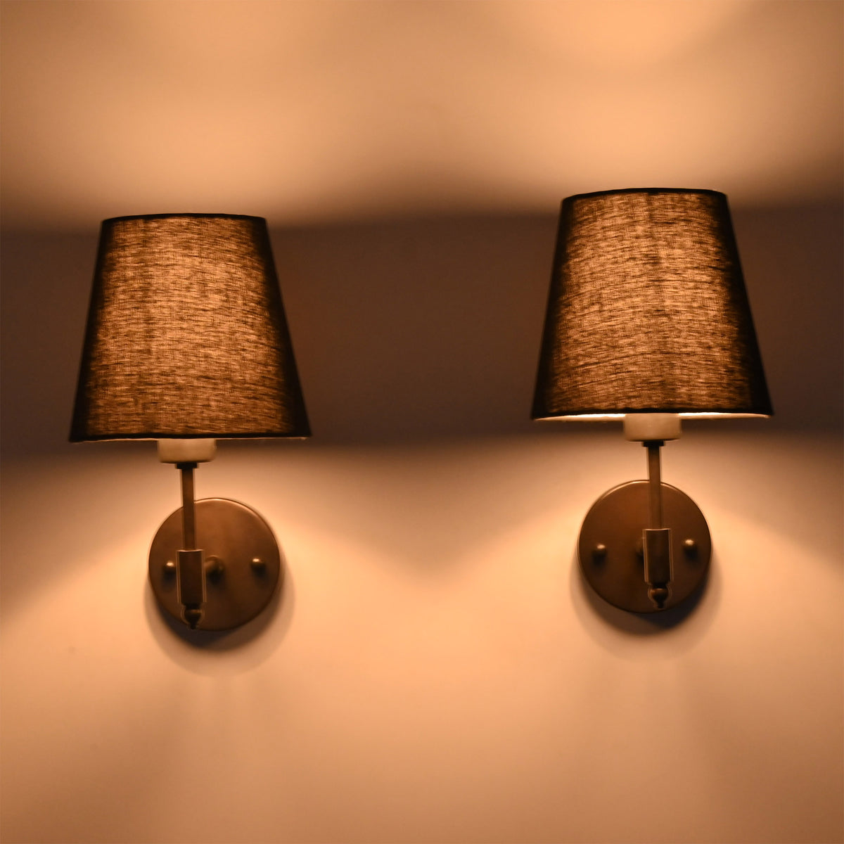 Illuminated Milan black shade wall sconces casting soft warm light upward and downward on the wall.