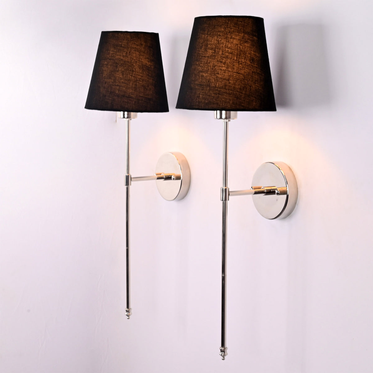 Angled view of Milan black shade chrome rod wall sconces with reflective round backplates and warm glow.