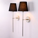 Angled view of Milan black shade chrome rod wall sconces with reflective round backplates and warm glow.