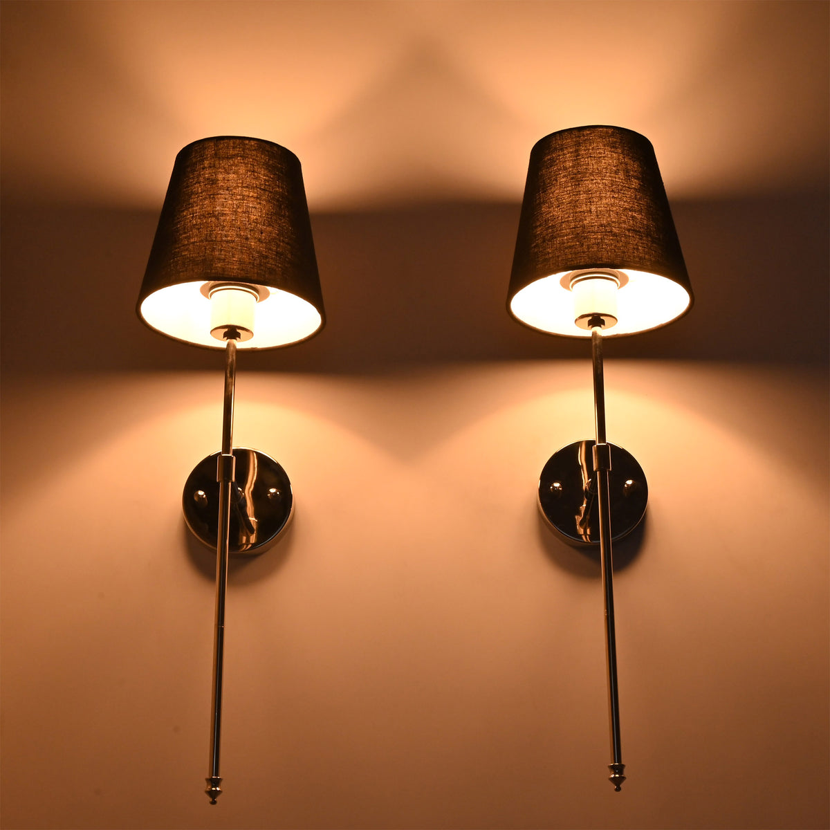 Illuminated Milan black shade chrome wall sconces with fabric shades and warm upward wall glow.