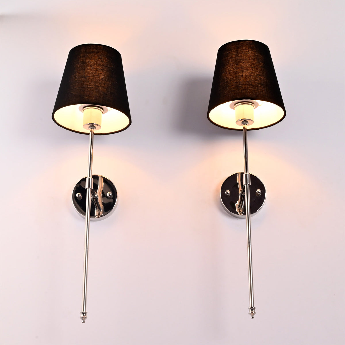 Low angle view of black shade chrome wall sconces showing warm light from beneath the shades.