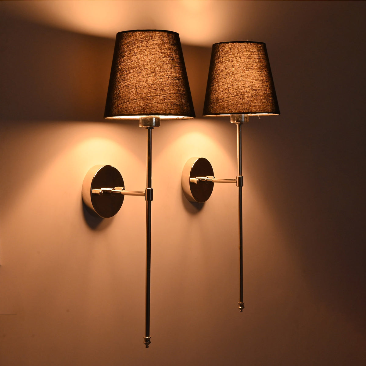 Warm angle view of black shade chrome rod wall sconces creating soft ambient wall illumination.
