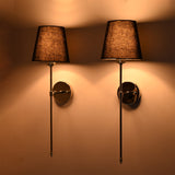 Front pair view of black shade chrome rod sconces glowing warmly with polished round wall plates.