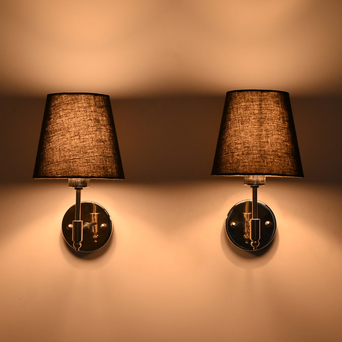 Illuminated Milan polished chrome wall sconce with black tapered fabric shade casting a warm ambient glow against the wall.