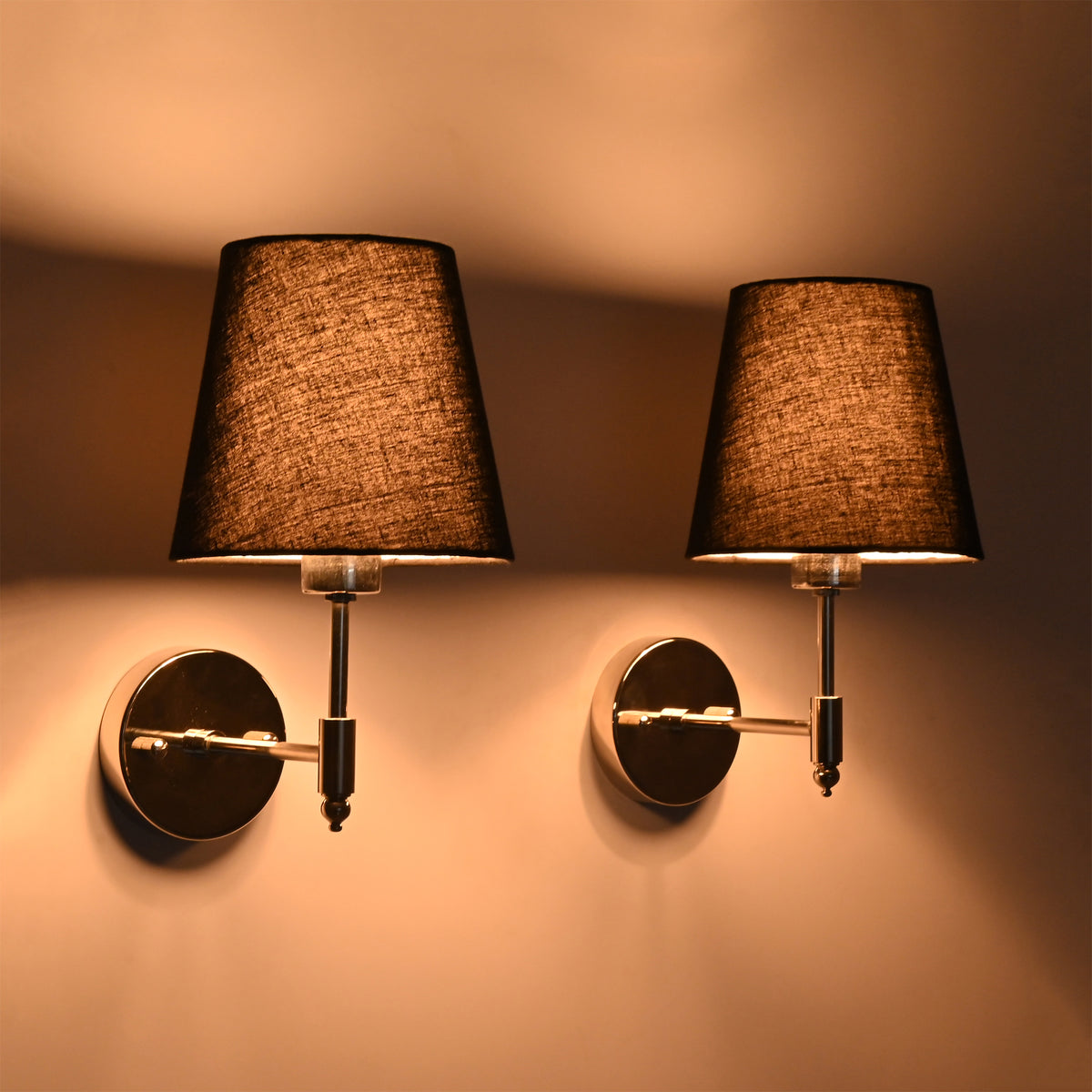 Side perspective of illuminated Milan polished chrome wall sconce with black tapered shade showcasing its warm ambient lighting effect.