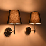 Side perspective of illuminated Milan polished chrome wall sconce with black tapered shade showcasing its warm ambient lighting effect.