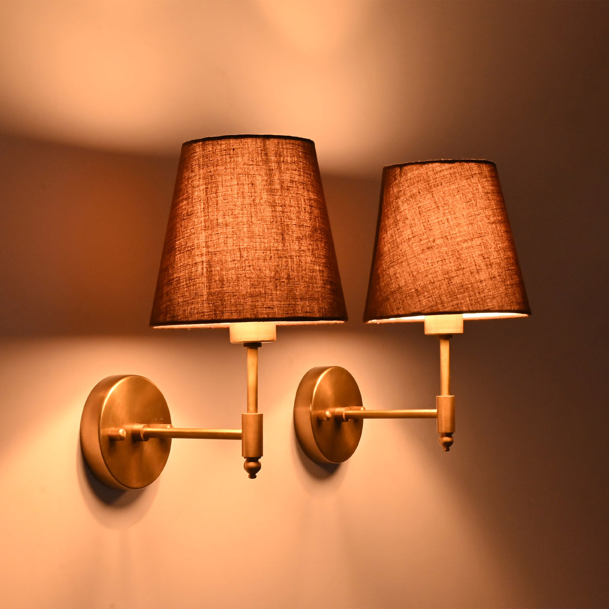Angled view of illuminated Milan Brown Shade Antique Brass Short Wall Sconce with warm antique brass finish.