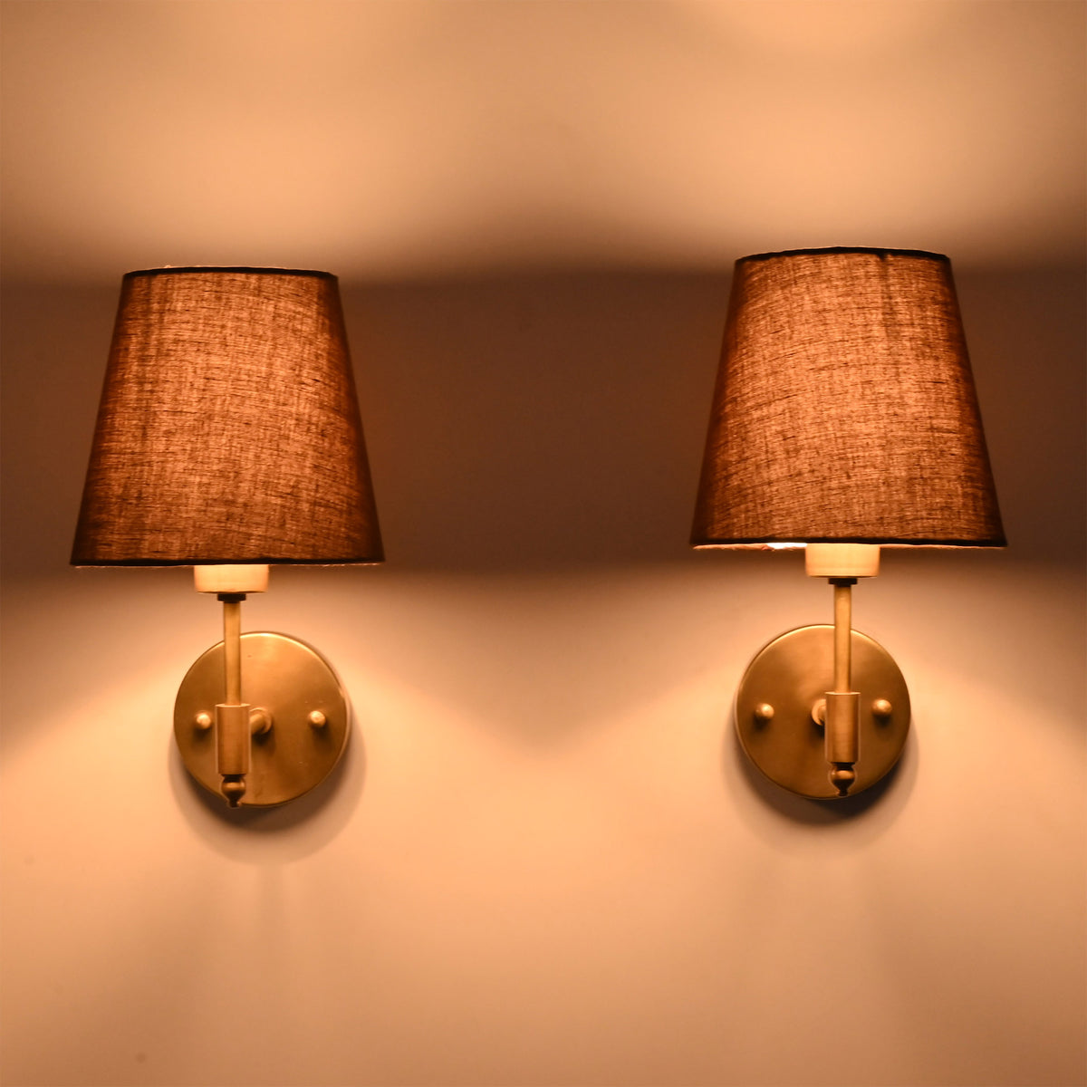Pair of illuminated Milan Brown Shade Antique Brass Short Wall Sconces creating warm ambient lighting on a wall.