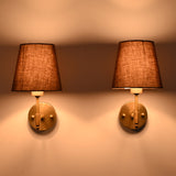 Pair of illuminated Milan Brown Shade Antique Brass Short Wall Sconces creating warm ambient lighting on a wall.