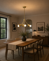 Milan 6 light satin brass Sputnik chandelier illuminated above a modern wooden dining table in a warm dining room interior.