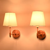 Angled illuminated view of the Milan copper antique brass wall sconce with a white fabric shade, highlighting its warm ambient lighting and handcrafted solid brass frame.