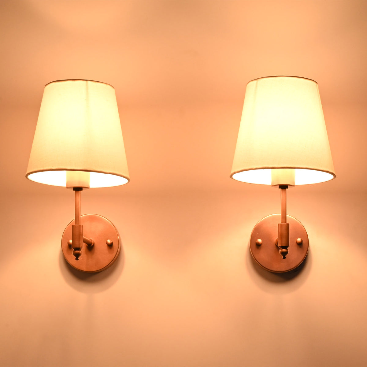 Illuminated Milan copper antique wall sconce with a white tapered fabric shade casting a soft warm glow, perfect for bedside lighting, hallways, and luxury residential interiors.