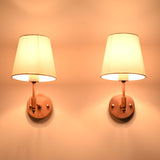 Illuminated Milan copper antique wall sconce with a white tapered fabric shade casting a soft warm glow, perfect for bedside lighting, hallways, and luxury residential interiors.