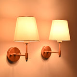 Pair of illuminated Milan copper antique wall sconces with white tapered fabric shades creating warm ambient lighting for bedrooms, living spaces, boutique hotels, and modern homes.