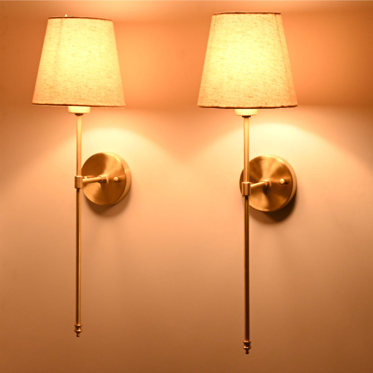 Angled pair of cream shade rod wall sconces with golden frame and warm ambient lighting effect.