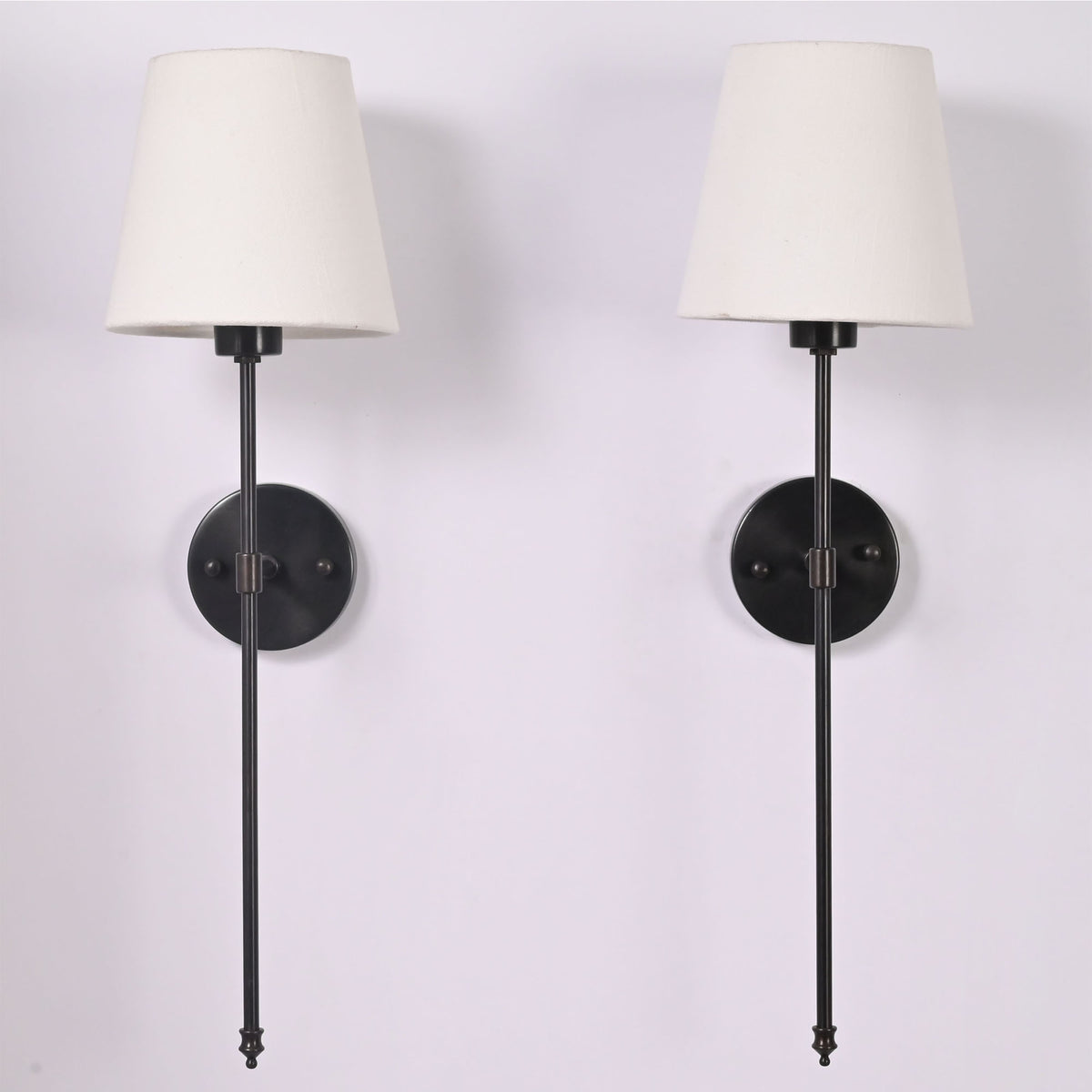 Front view of two ivory shade black rod wall sconces with round backplates and long vertical stems.