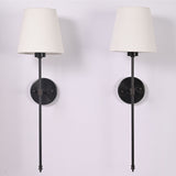 Front view of two ivory shade black rod wall sconces with round backplates and long vertical stems.